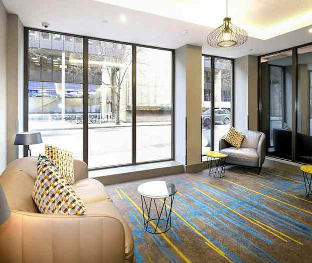 Rum med store glasvinduer, lænestole og små borde. (AI-genereret tekst)