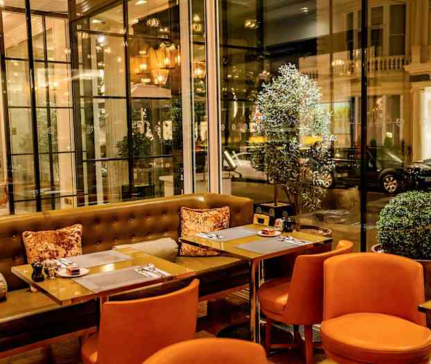 En restaurant med orange stole og glasvægge med udsigt til gaden. (AI-genereret tekst)