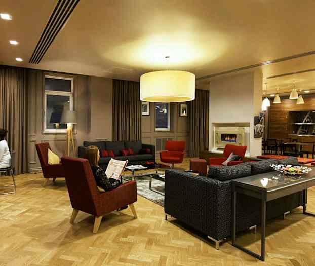 Et elegant opholdsområde med sofaer, lænestole og et sofabord omgivet af varm belysning og moderne indretning. (AI-genereret tekst)