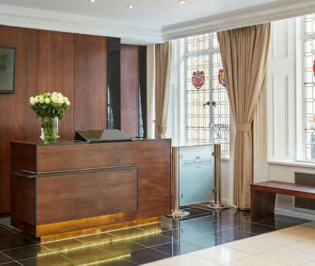 Hotelreception med et skranke af træ og en vase med hvide blomster, ved siden af vinduer med farvede dekorationer. (AI-genereret tekst)