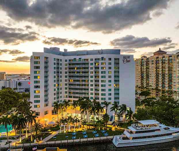 En bygning med altaner, en swimmingpool og en båd er synlige i forgrunden. Solnedgangen skaber en varm baggrund. (AI-genereret tekst)