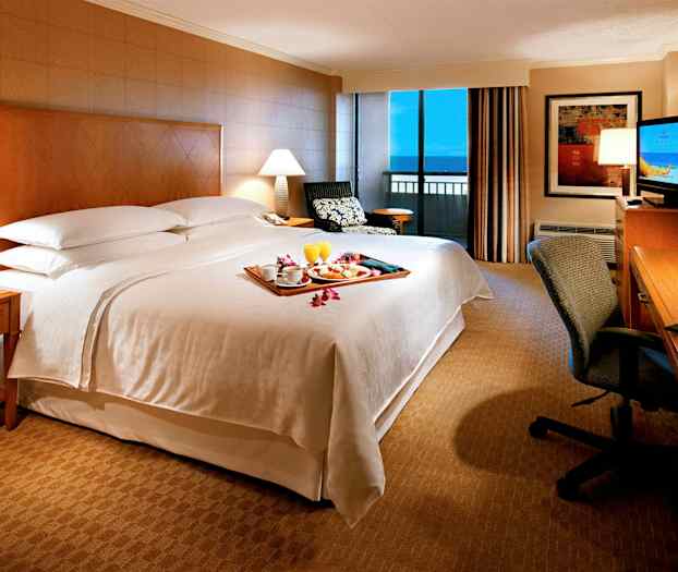 Et soveværelse på et hotelværelse med en stor seng, sidebord, skrivebord og vindue med udsigt. (AI-genereret tekst)