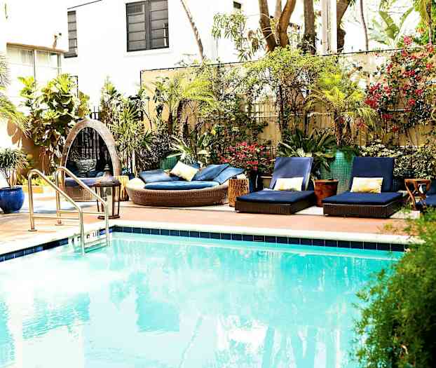 En udendørs swimmingpool med omkringliggende liggestole og beplantning. (AI-genereret tekst)