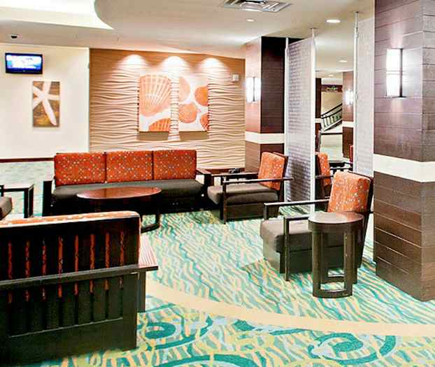 Et venteområde med farverigt tæppe, flere stole og sofaer med orange stof samt vægdekorationer. (AI-genereret tekst)