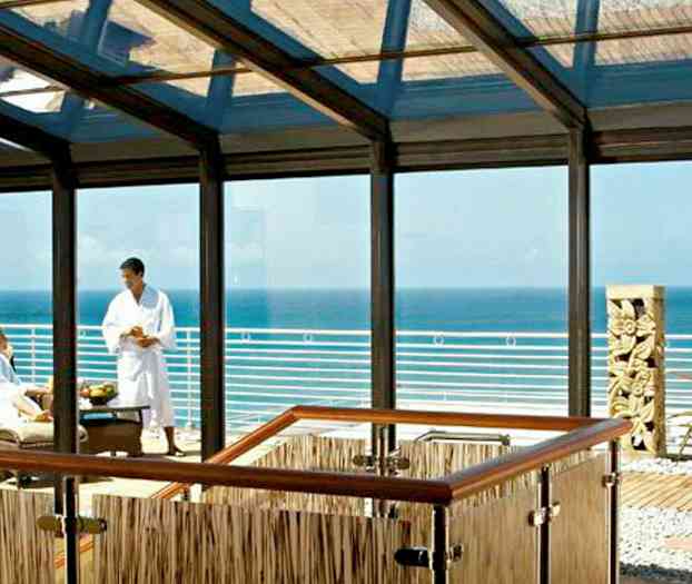 En indglaset lounge med udsigt over havet og en terrasse med en skulptur og planter. (AI-genereret tekst)