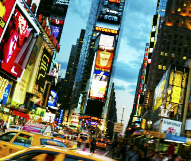 Trafikeret gade med taxier og reklamebeklædte bygninger i et bymiljø. (AI-genereret tekst)