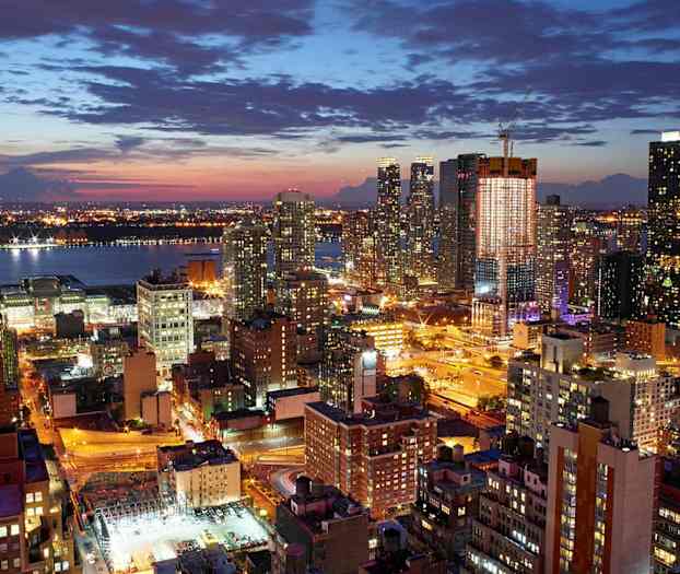 Et natlig bymiljø med flere oplyste bygninger og gader, med en flod i baggrunden. (AI-genereret tekst)