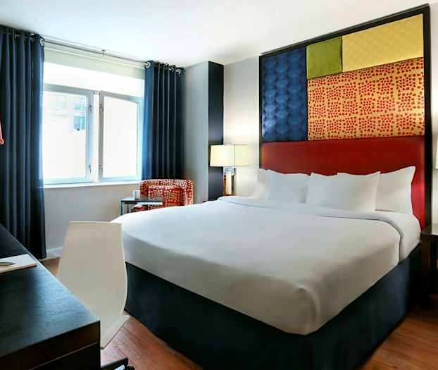 Hotelværelse med en stor seng, mørke gardiner, skrivebord og farverig vægdekoration. (AI-genereret tekst)