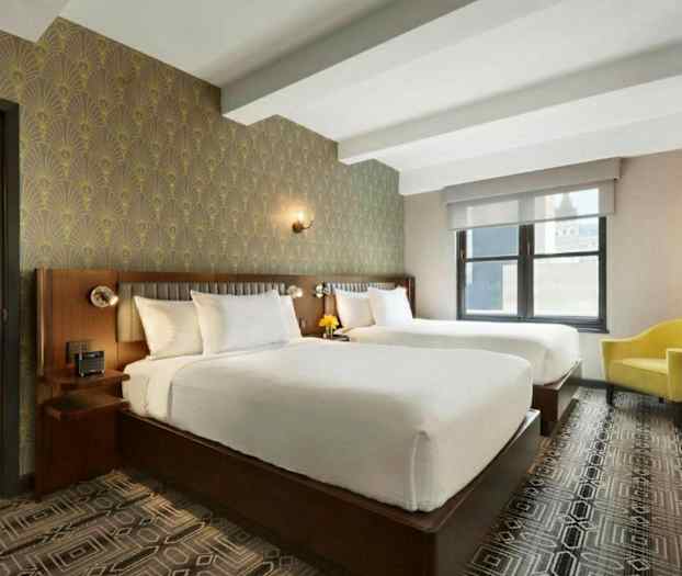 Et hotelværelse med to store senge, en gul lænestol, dekorative tapeter og et vindue. (AI-genereret tekst)