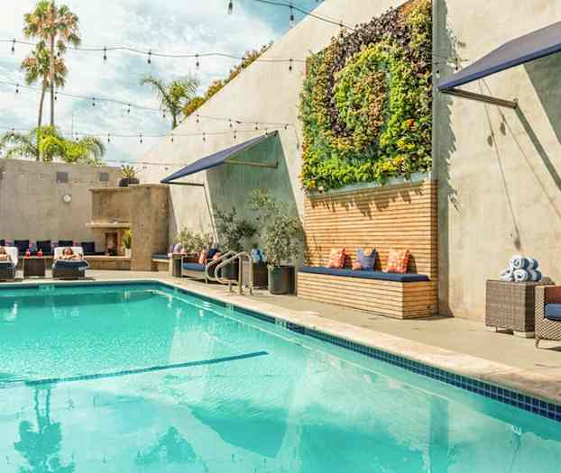 En udendørs pool med liggestole, grønne planter på væggen og siddepladser med puder. (AI-genereret tekst)