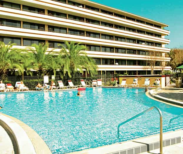 Billede af en udendørs swimmingpool foran et fler-etagers hotel. (AI-genereret tekst)
