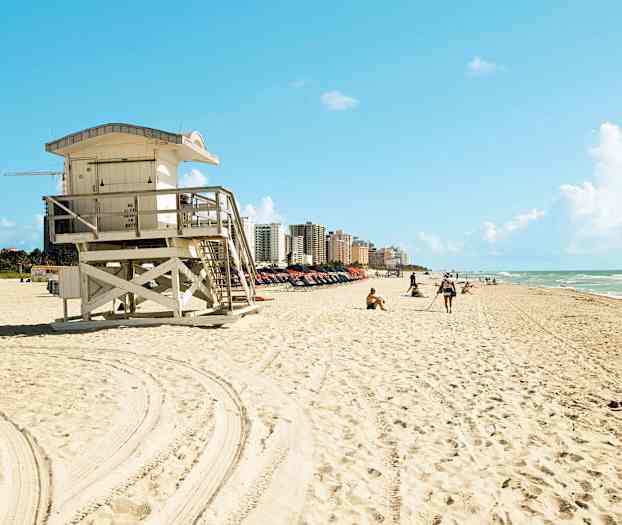 En strand med et livreddertårn i forgrunden og bygninger i baggrunden. (AI-genereret tekst)