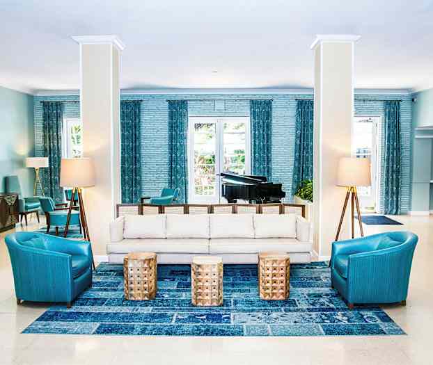 Et interiørbillede af en hotellobby med siddeområde, sofaer, lænestole og borde samt et flygel i baggrunden. (AI-genereret tekst)