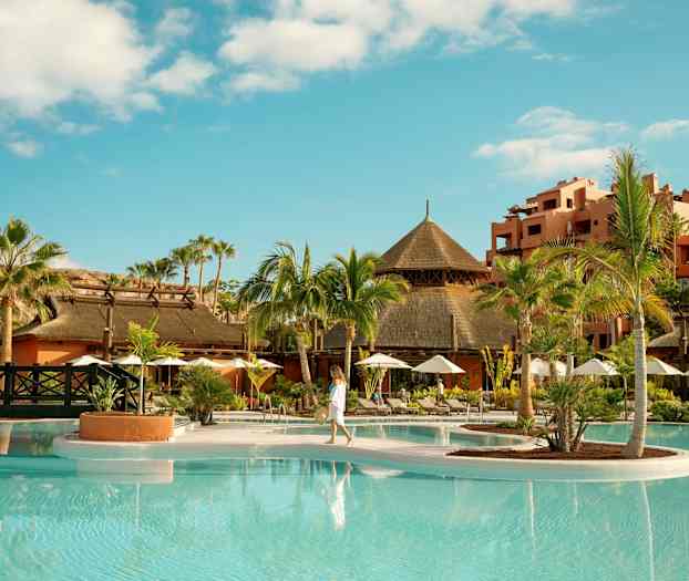 Tropisk resort med palmer, pool og traditionelle bygninger. (AI-genereret tekst)