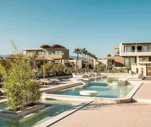 Et luksuriøst resort med pool, liggestole og moderne bygninger under en klar himmel. (AI-genereret tekst)