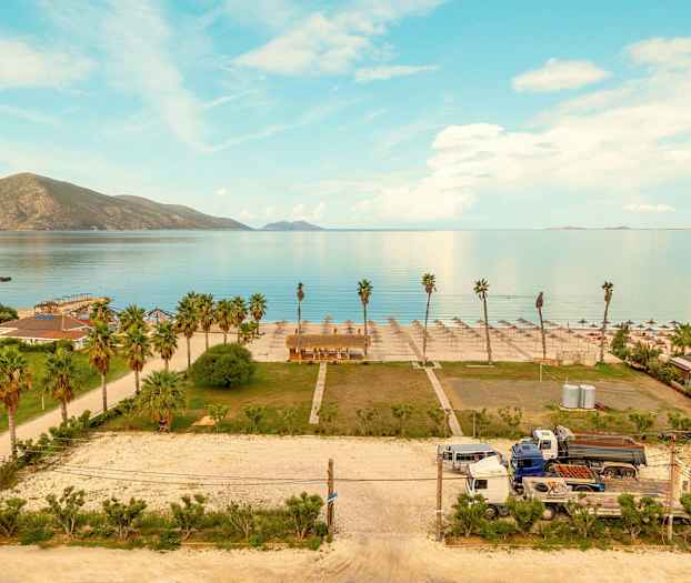 Udsigt over en strand med parasoller og palmer, nogle bygninger og køretøjer ses også. (AI-genereret tekst)