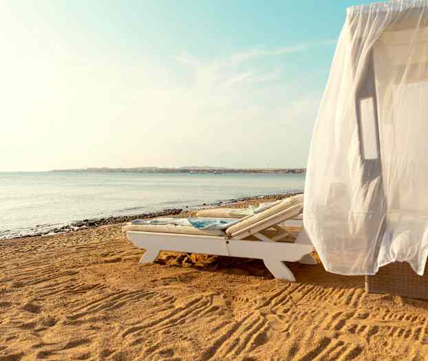 En solseng med et hvidt draperi på en sandstrand ved havet. (AI-genereret tekst)