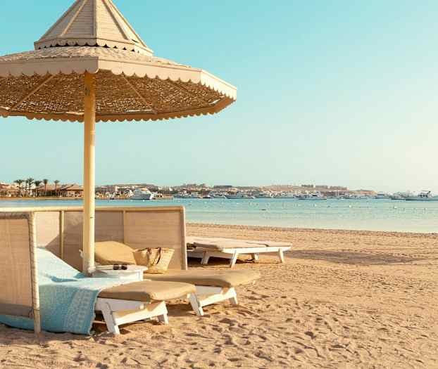 En strand med solsenge og parasoller, samt både på havet. (AI-genereret tekst)