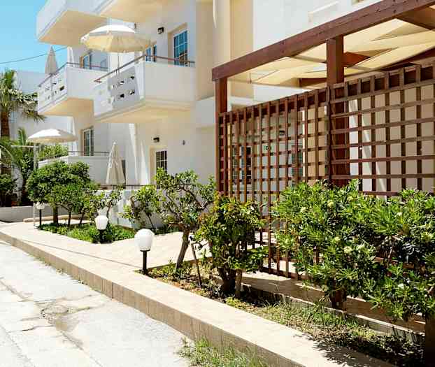 En gade med hvide bygninger, grønne buske og parasoller. (AI-genereret tekst)