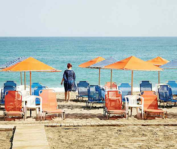 Strand med liggestole og parasoller, en person går mod havet. (AI-genereret tekst)