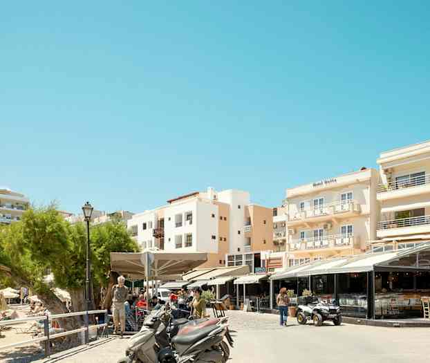 Billede af en gade med restauranter og motorcykler foran bygninger i et solrigt område. (AI-genereret tekst)