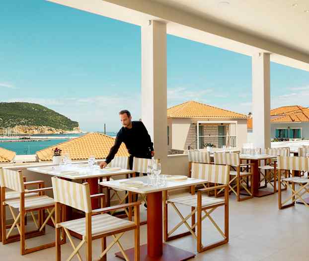 Restaurant med bordopstilling, udsigt over havet og terrasse, med baggrund af terrakottatag og en frodig bakke. (AI-genereret tekst)