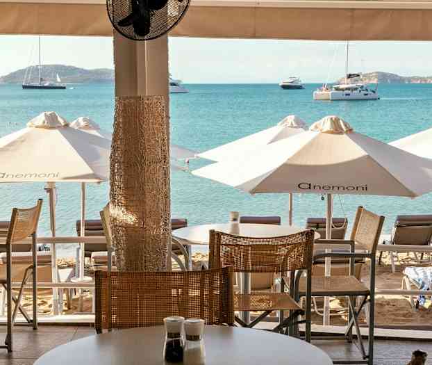 Udsigt fra en terrasse mod stranden med liggestole, parasoller og havet i baggrunden. (AI-genereret tekst)