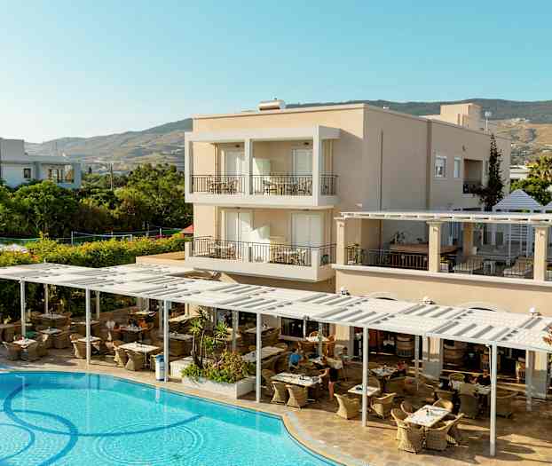 En hotelbygning med altaner, en udendørs restaurant og en swimmingpool i forgrunden. (AI-genereret tekst)