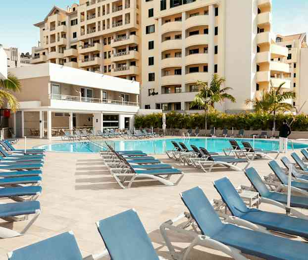 Udendørs pool med liggestole og omkringliggende bygninger. (AI-genereret tekst)