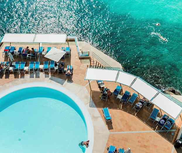 Liggestole og en pool ved havet set fra oven. (AI-genereret tekst)