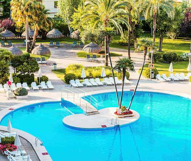 En pool omgivet af liggestole og parasoller, med palmer og grøn beplantning i baggrunden. (AI-genereret tekst)