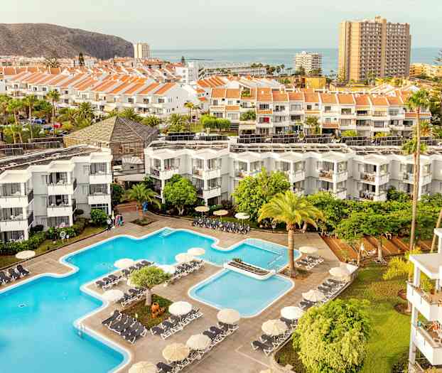 Udsigt over hotelområde med pools, bygninger og omkringliggende landskab. (AI-genereret tekst)