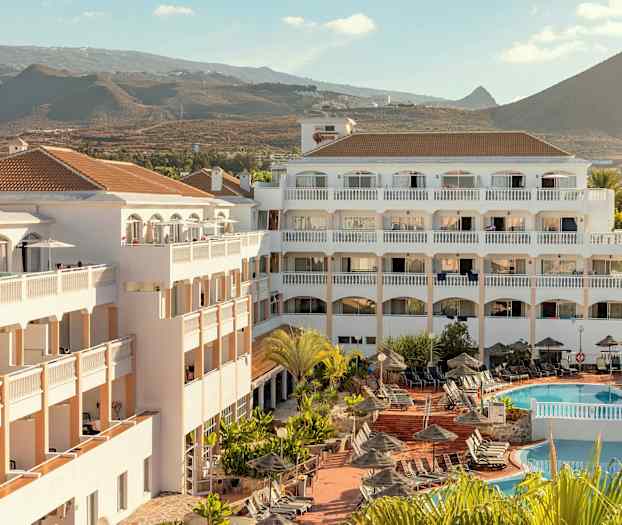 Hotelbygning med poolområde og liggestole, omgivet af bjerglandskab. (AI-genereret tekst)