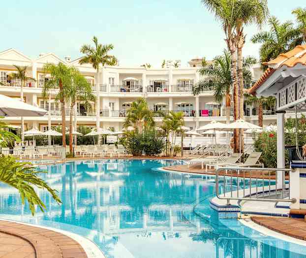 Billede af et hotel med en pool, omgivet af liggestole, parasoller og beplantning. (AI-genereret tekst)