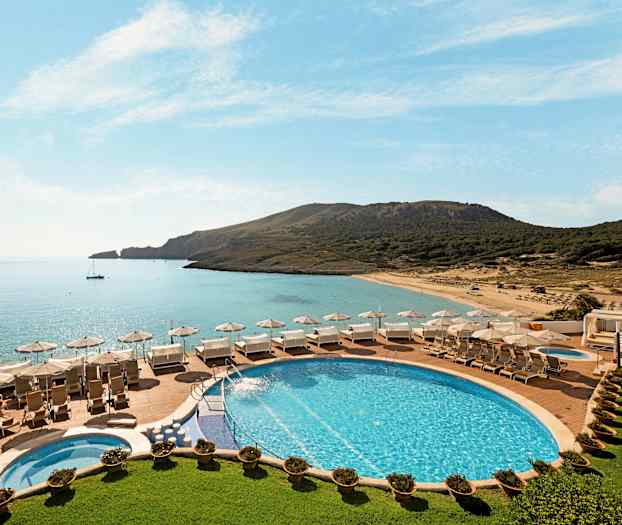 Poolområde med liggestole og parasoller med udsigt over en strand og havet. (AI-genereret tekst)