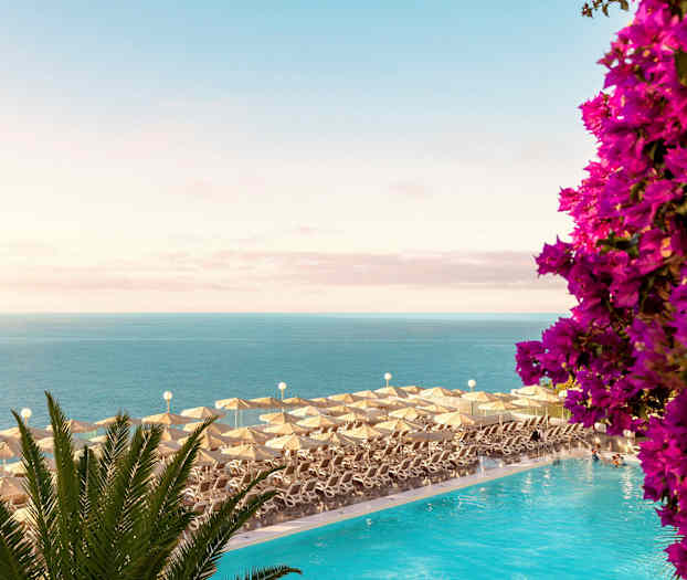 Liggestole med parasoller ved en pool med udsigt over havet og blomster. (AI-genereret tekst)