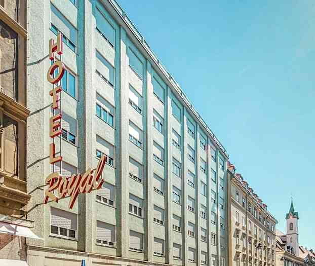 Billede af en bygade med hotellets facade og omkringliggende bygninger. (AI-genereret tekst)