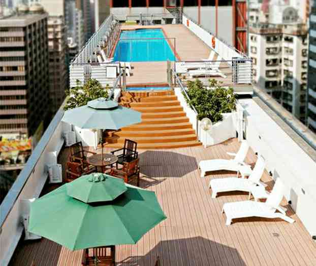 En tagterrasse med solsenge, spiseborde og parasoller samt en pool i baggrunden. (AI-genereret tekst)