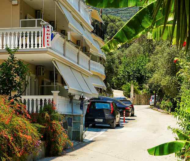 En bygning med altaner og markiser ved en vej med parkerede biler og grønt. (AI-genereret tekst)