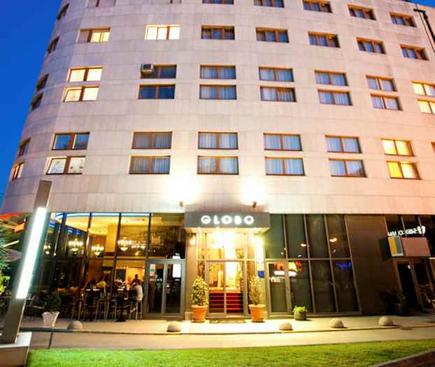 Et hotel med oplyst facade og indgang, fotograferet i skumringen. (AI-genereret tekst)