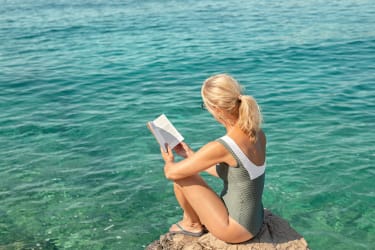 Kvinde sidder alene og læser en bog ved vandet