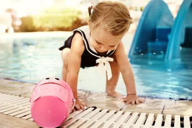 Lille pige leger med en spand ved poolkanten på Family Garden