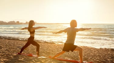 Kvinde og mand dyrker yoga på stranden