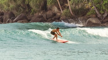 surfer i vandet med palmer i baggrunden
