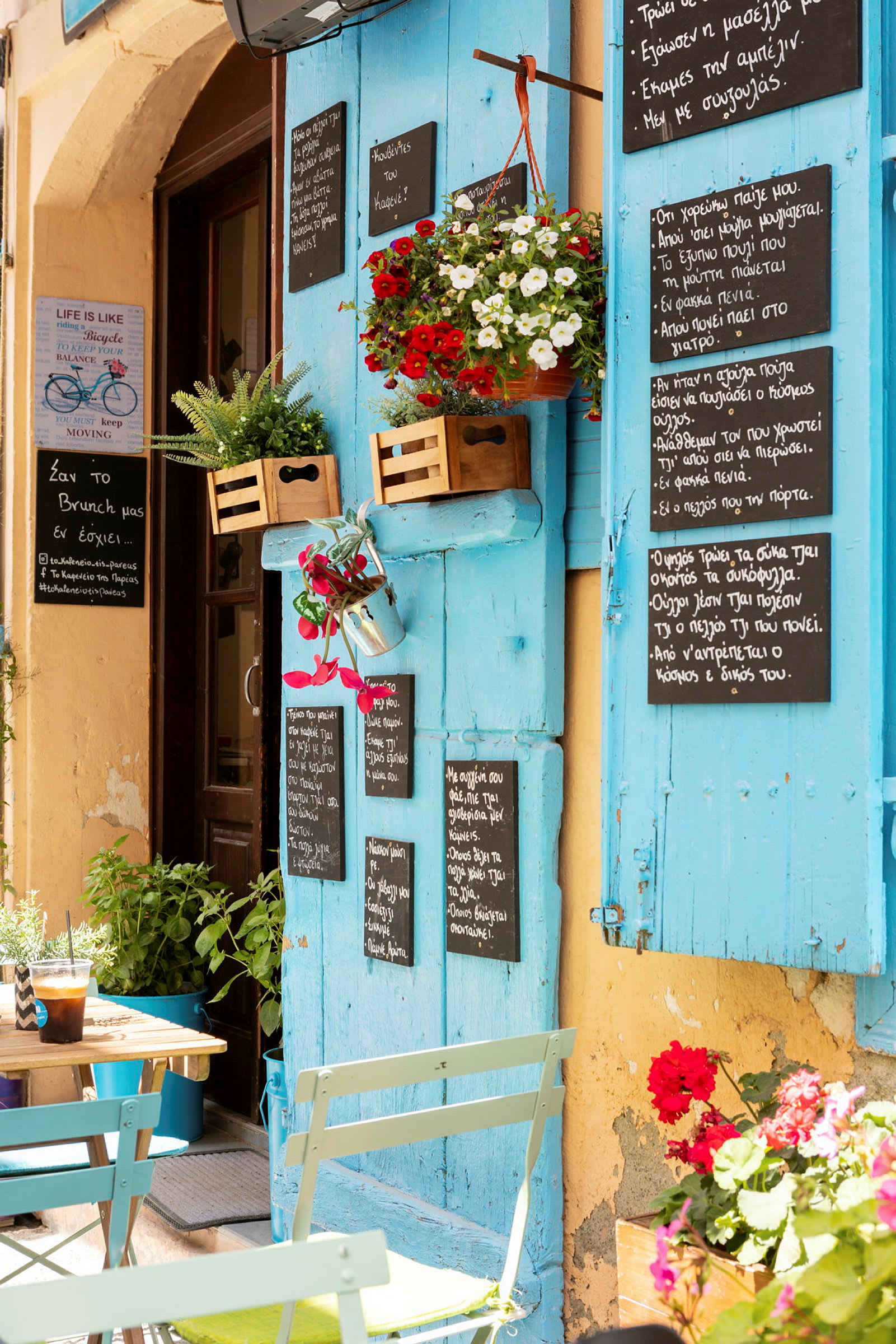 Et farverigt cafémiljø med blå skodder, tavler med tekst og blomster. (AI-genereret tekst)