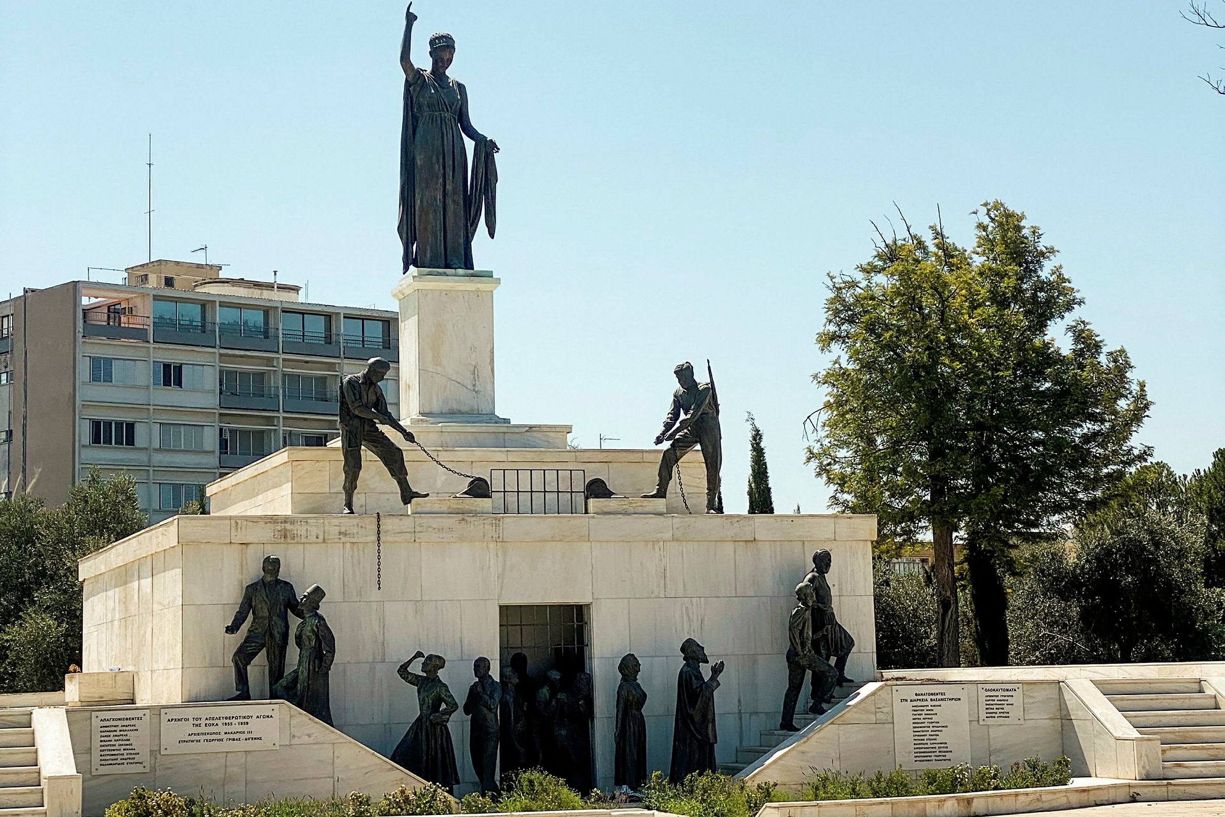 Et monument i sten og bronze med flere skulpturer, der forestiller personer og en kvinde med en løftet hånd. (AI-genereret tekst)