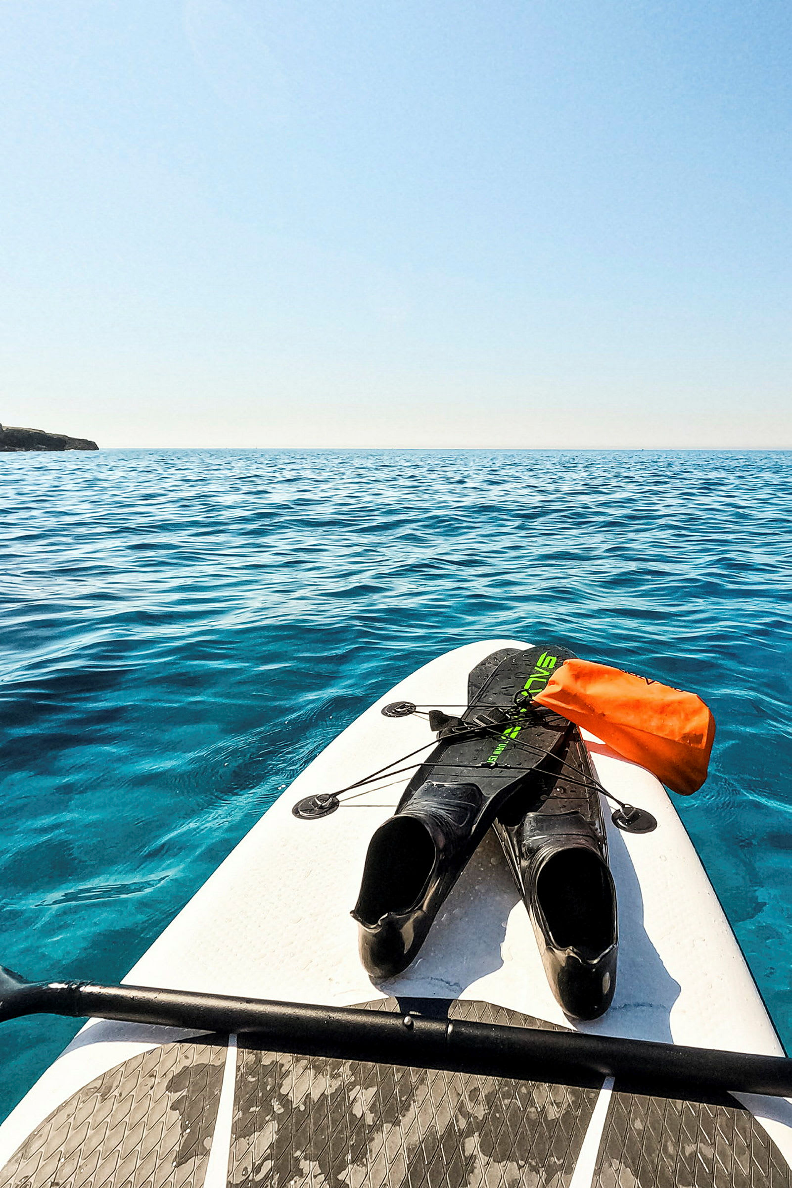 Et paddleboard med svømmefødder og en orange vandtæt pose fotograferet på et roligt hav. (AI-genereret tekst)