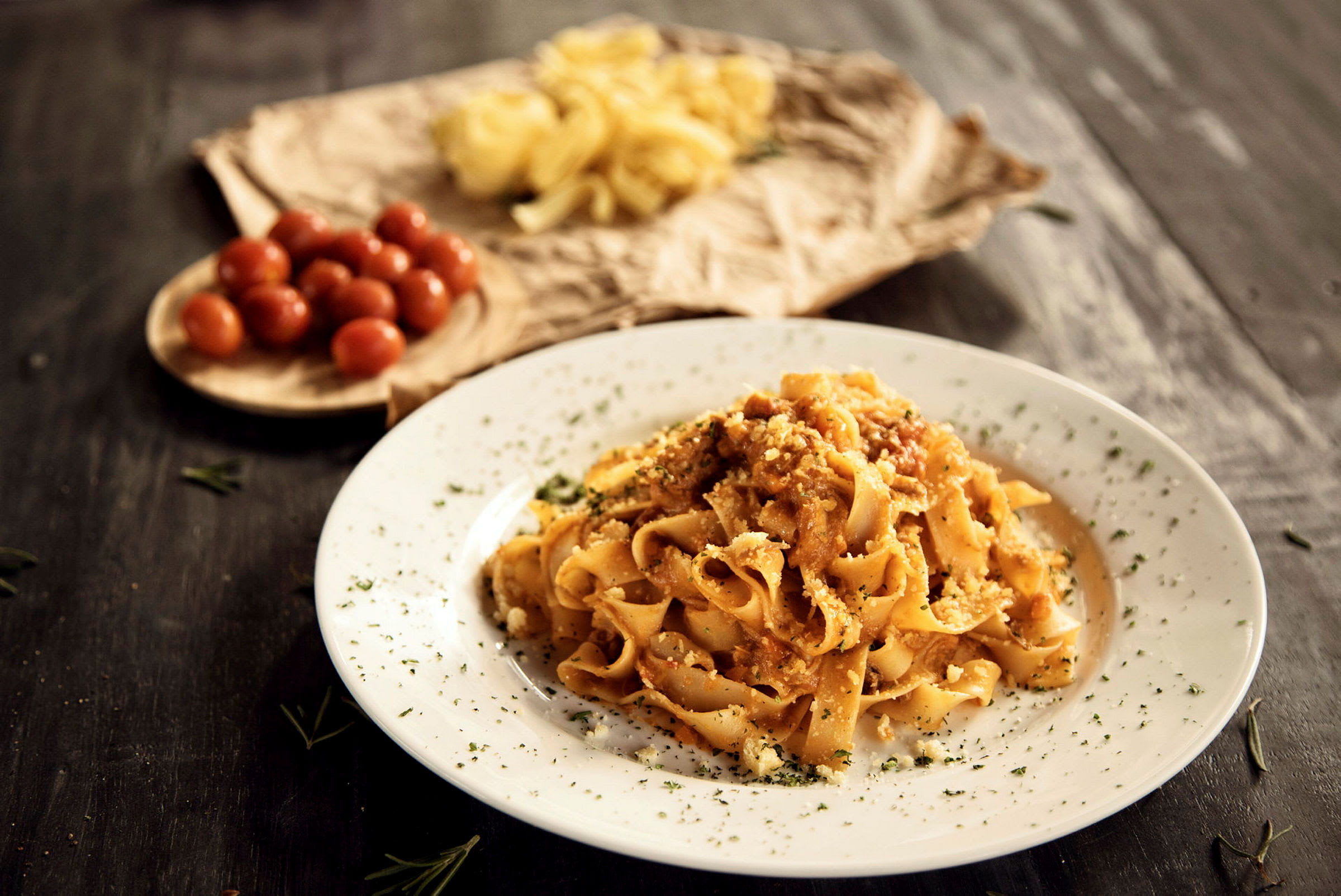 En tallerken med pasta toppet med sauce og urter, med cherrytomater og rå pasta i baggrunden. (AI-genereret tekst)