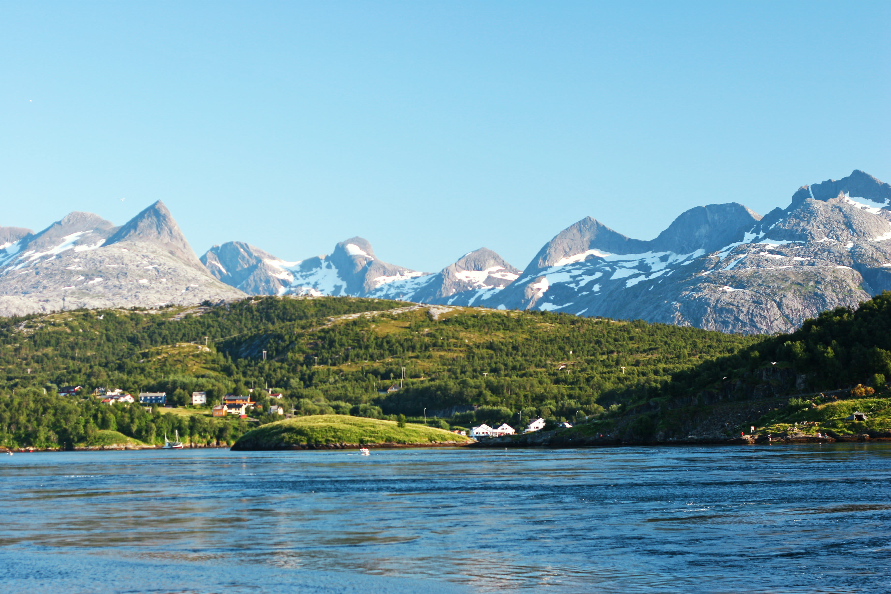 En udsigt over et bjerglandskab med snedækkede toppe, grønt landskab og huse ved en vandflade. (AI-genereret tekst)