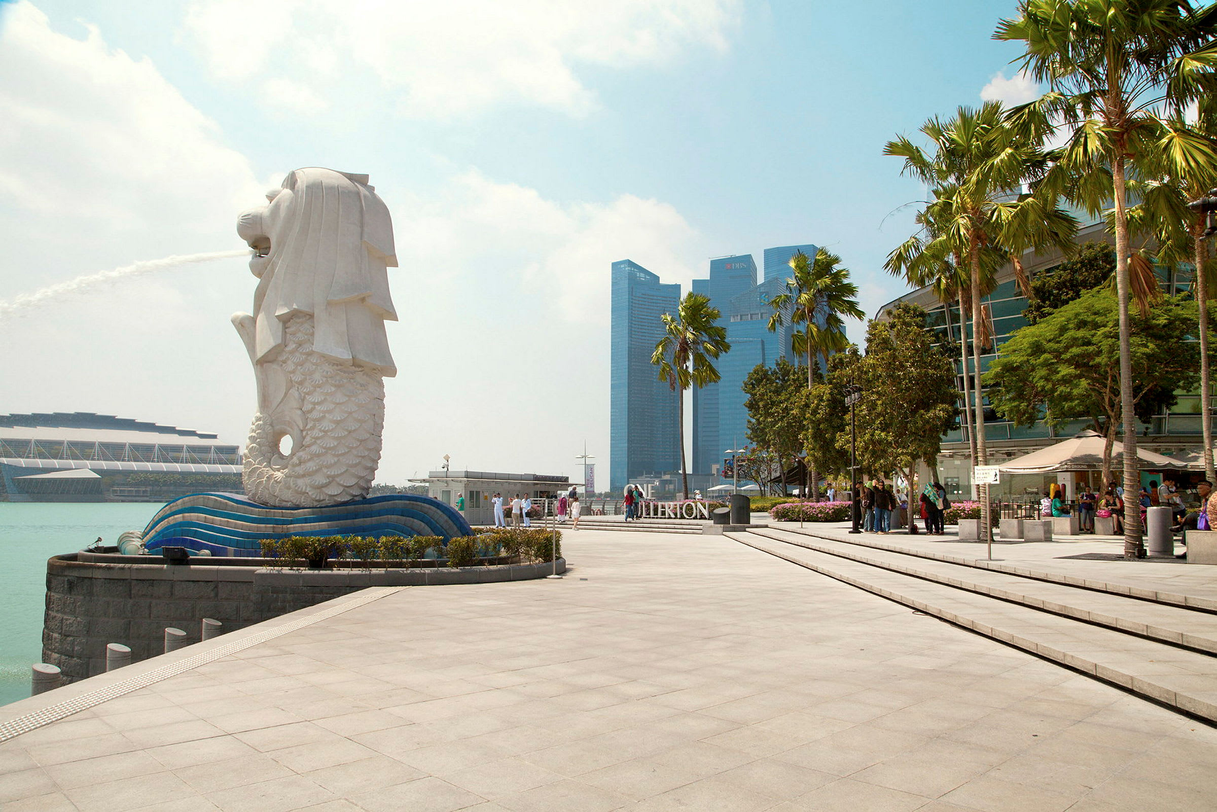 Billede af Merlion-statuen i Singapore med fontæne, omgivet af moderne arkitektur og palmer. (AI-genereret tekst)